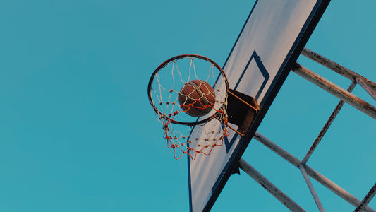 A basketball shoots in the ring under clear blue sky.