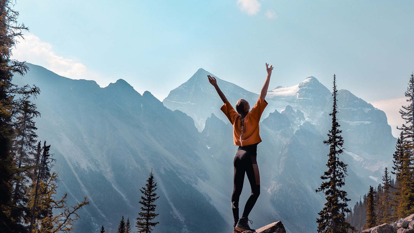 woman standing on rock with arms raised looking at mountains