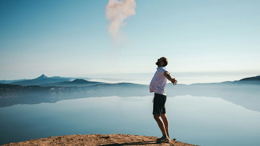 man standing while spreading arms beside calm body of water
