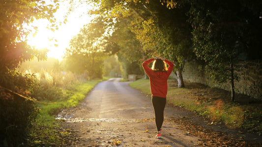 woman in tracksuit walks along a tree lined road in the sun