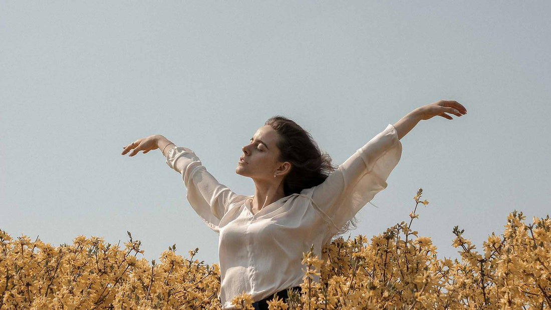 woman in a flower field raising her hands while soaking under the daylight