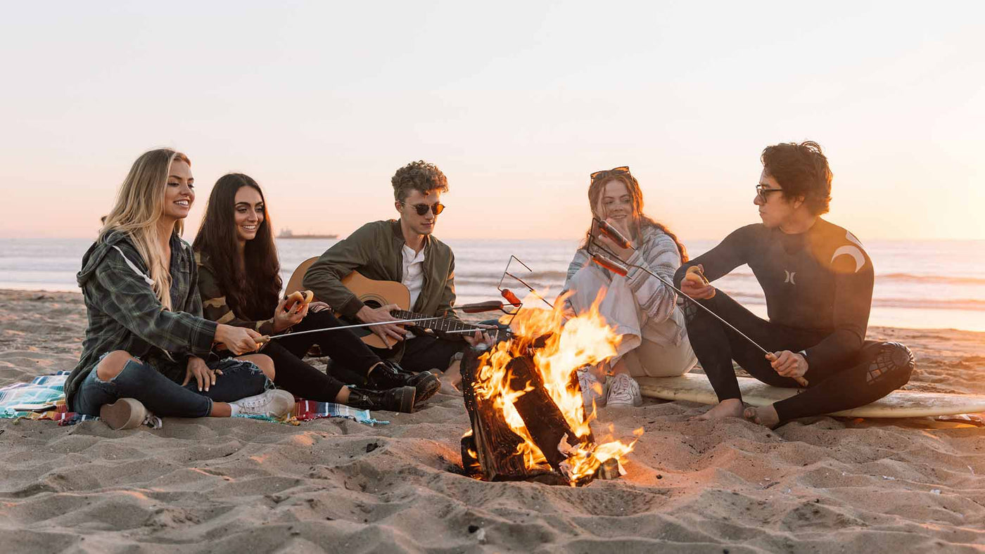 five people sitting on the beach around a bonfire