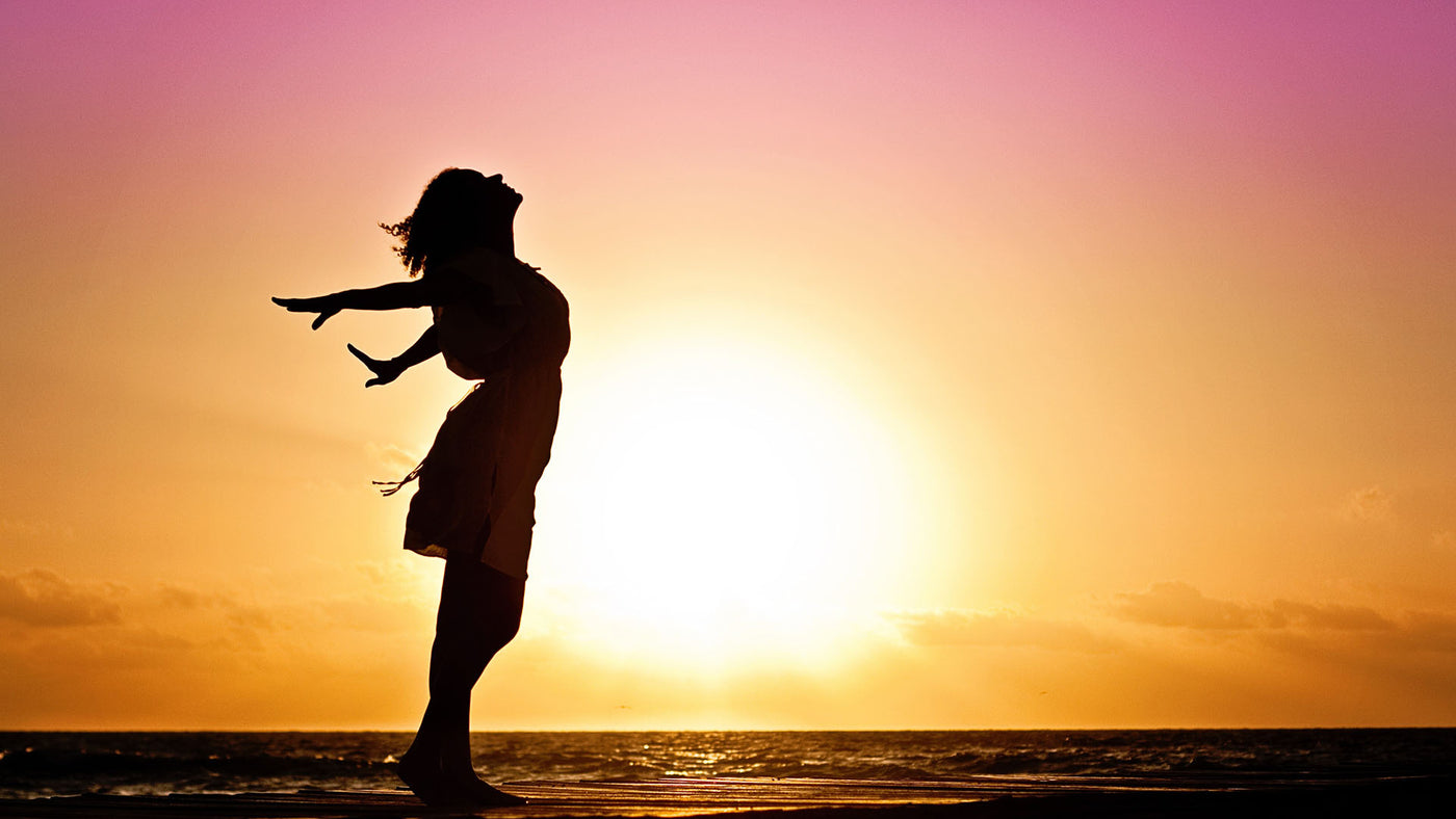 a silhouette of a woman with outstretched arms in front of a sunrise