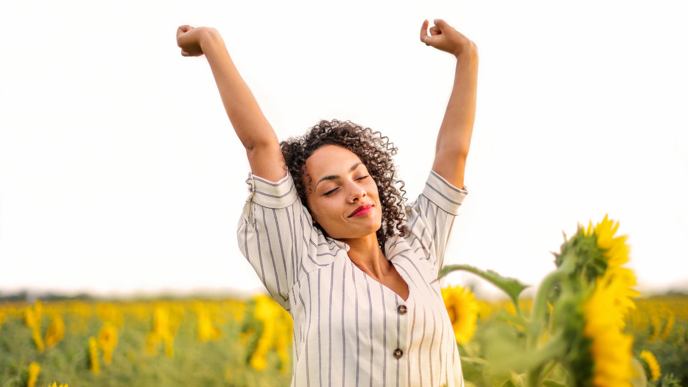 A woman putting her hands up in the air while in the middle of a sunflower field.