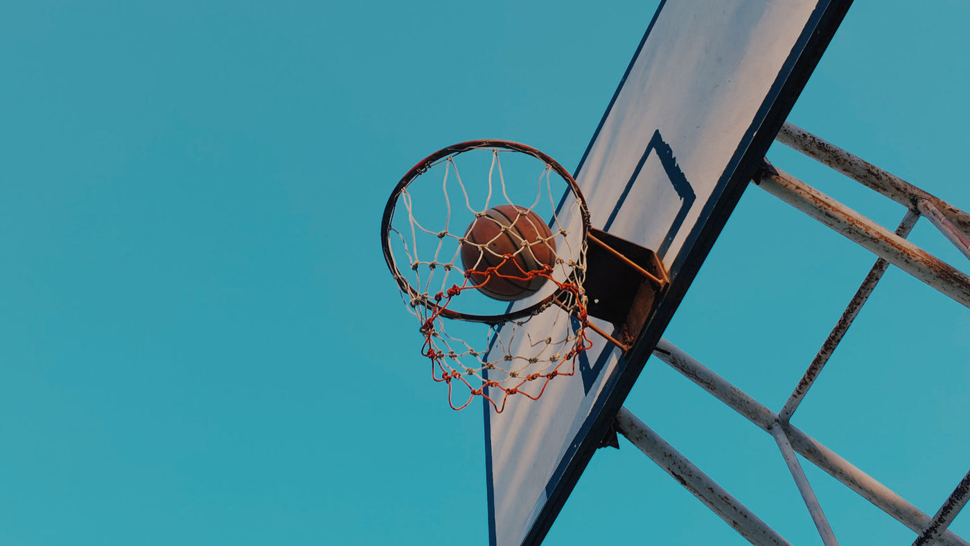 A basketball shoots in the ring under clear blue sky.
