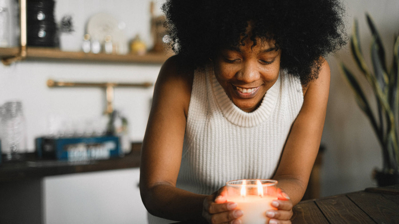 A woman of color smiles while holding a lighted candle on the table.