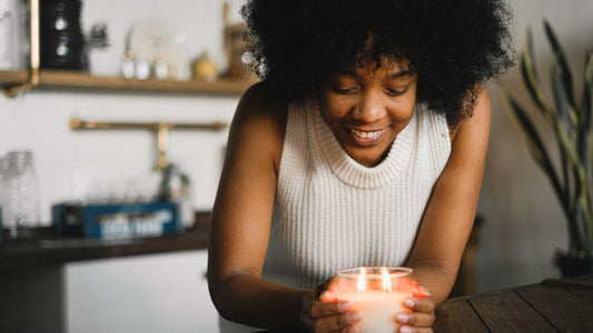 A woman of color smiles while holding a lighted candle on the table.