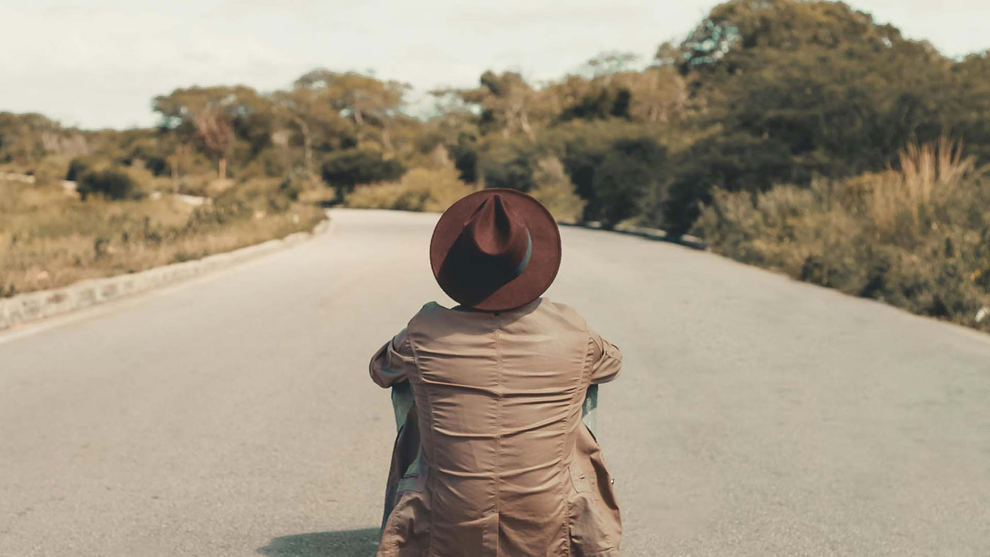 man wearing hat sitting on ground in the middle of a road