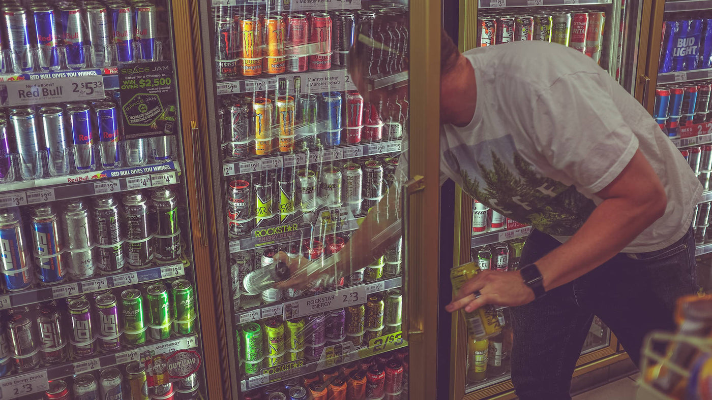 A man getting a drink from the store refrigerator full of energy drinks.
