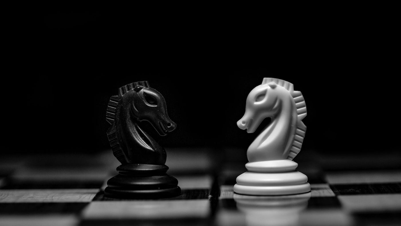 A black and a white ceramic knight chess piece facing each other.