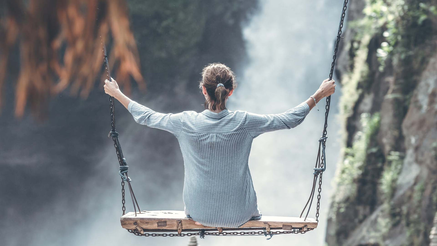 a woman sitting on a swing overlooking a waterfall