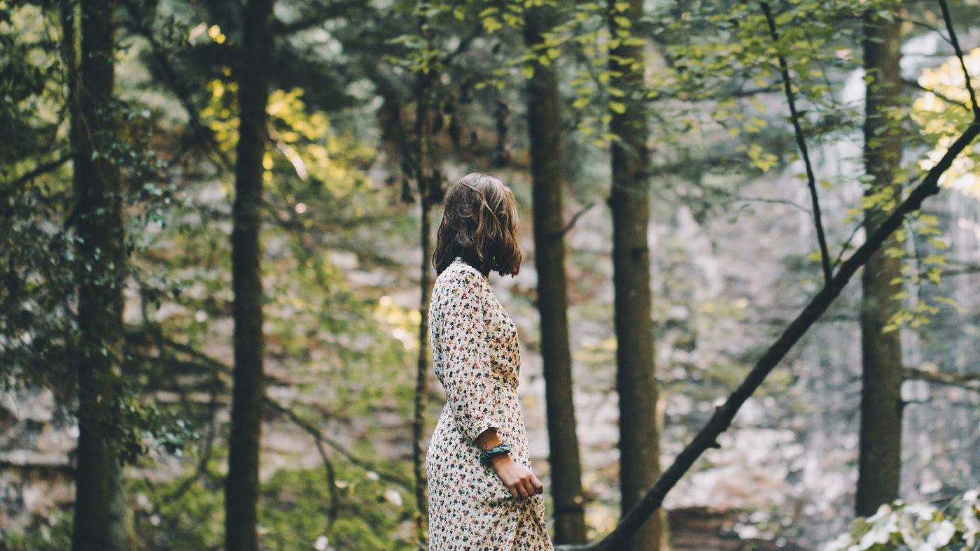 a woman standing and looking at the trees in the middle of forest