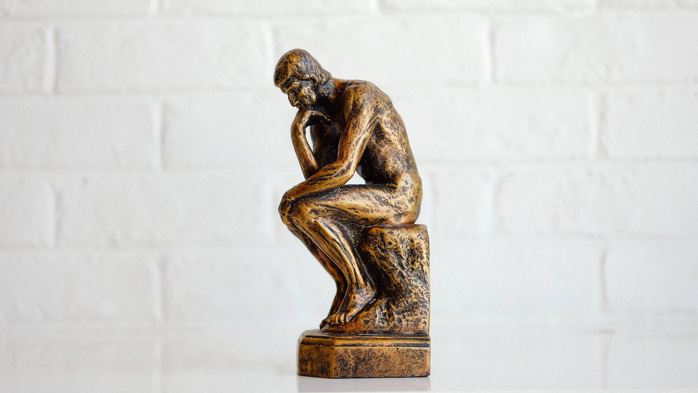 A golden mini The Thinker statue figurine on a white tile background.