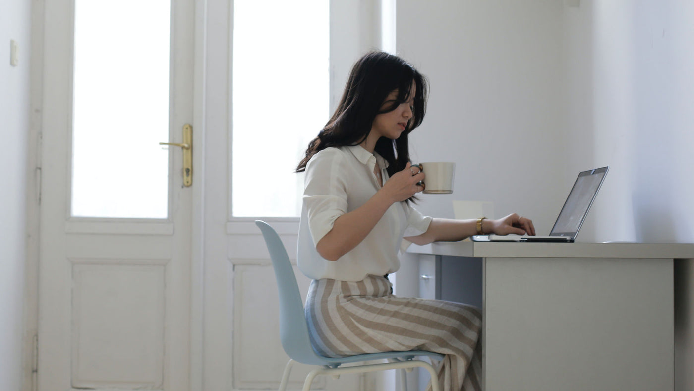 A young woman drinking coffee while working at home.