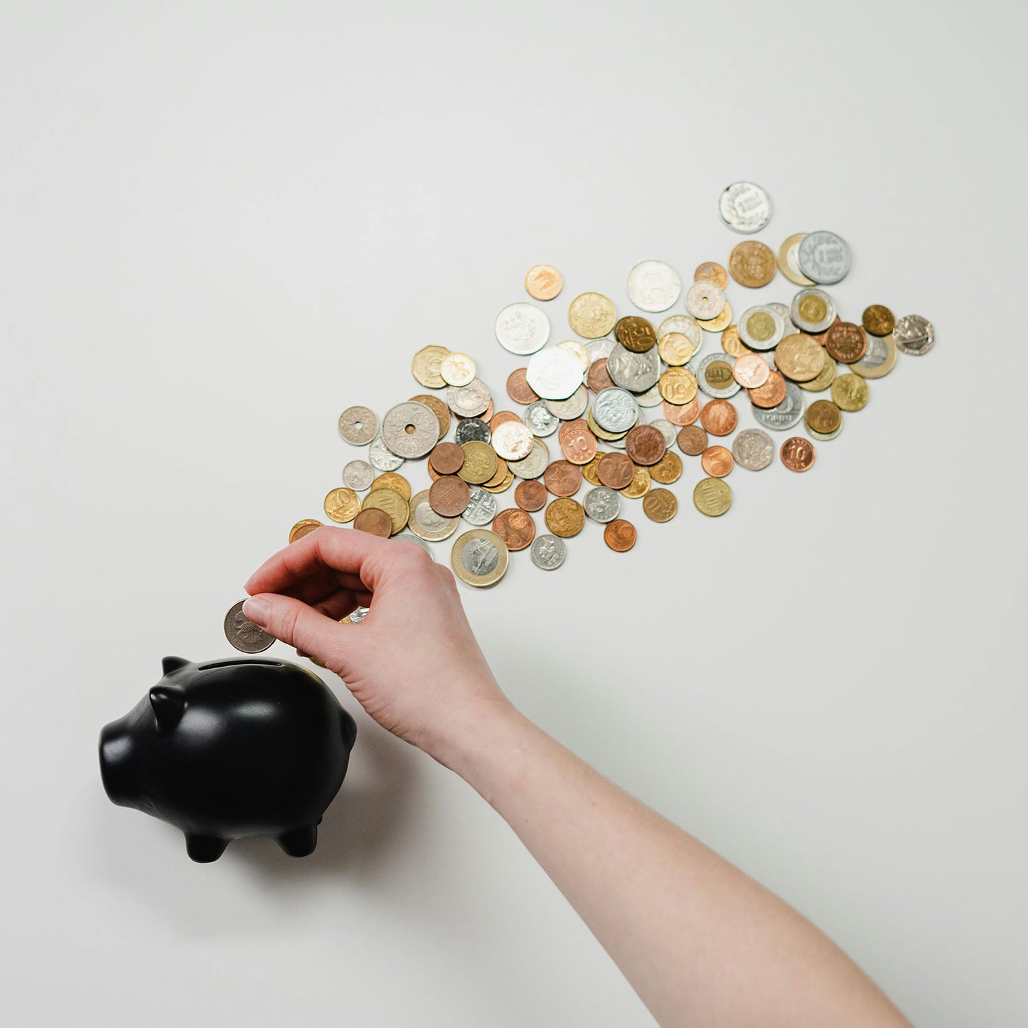 assorted coins with a person's hand putting a coin into a piggy bank