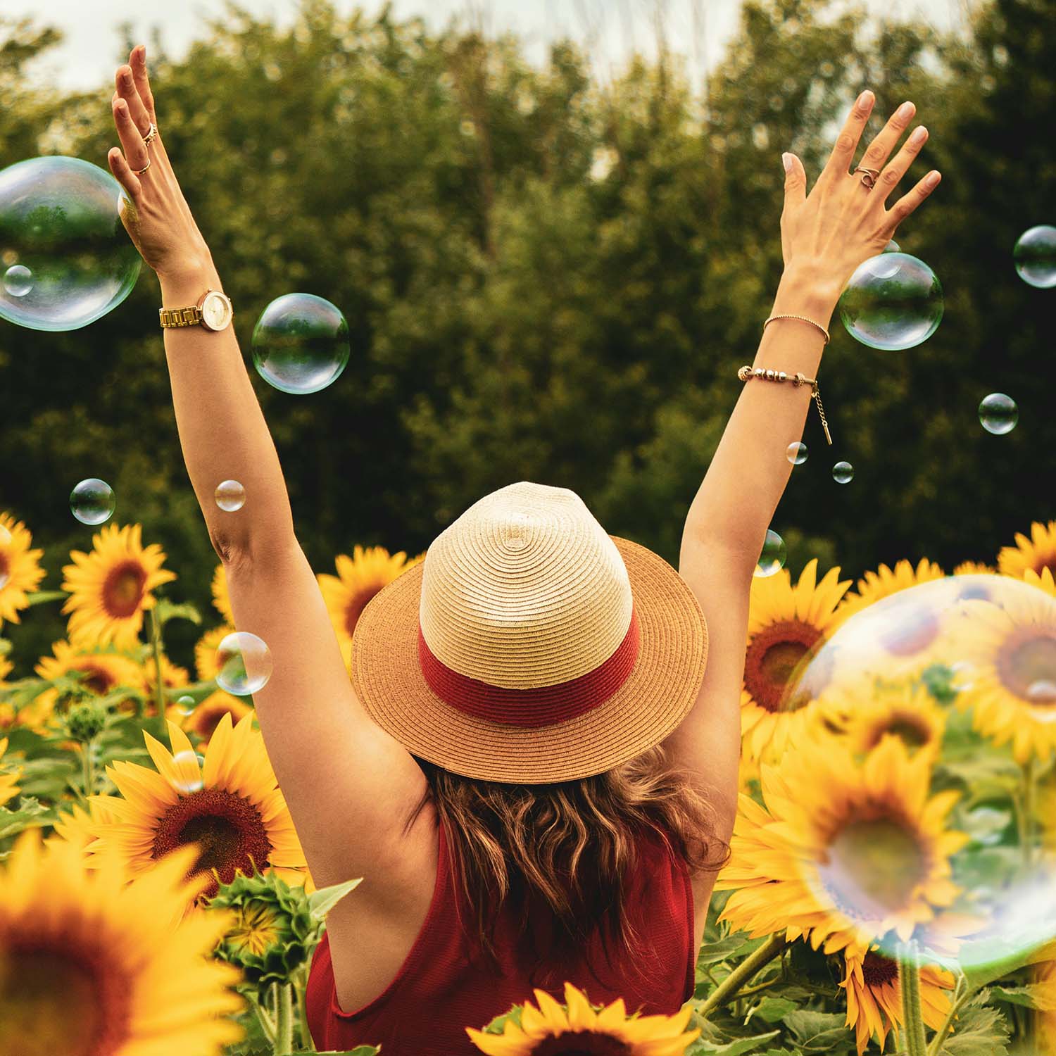 woman in a hat standing in a sunflower field with bubbles and arms raised