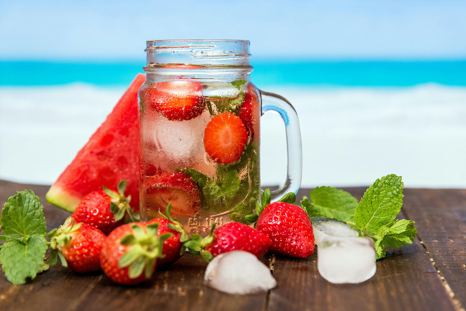 mason jar on a table with watermelon, strawberries, and mint