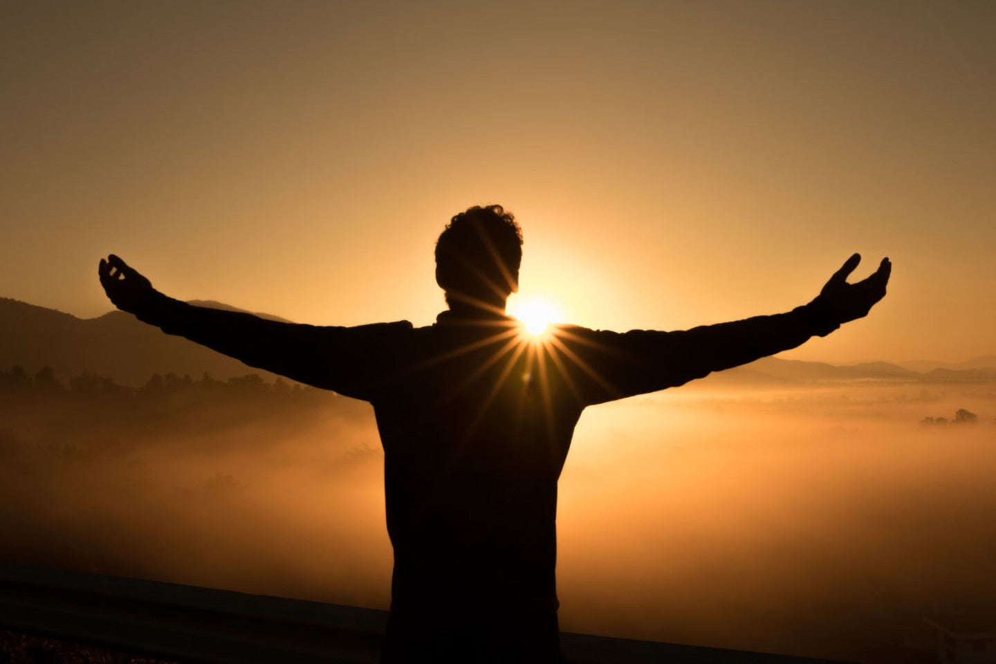 man with arms outstretched at sunset