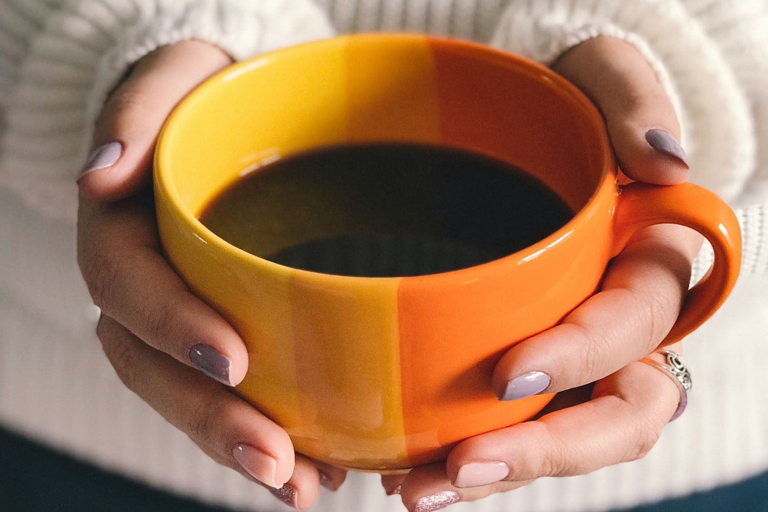 Woman holding an orange cup filled with black coffee