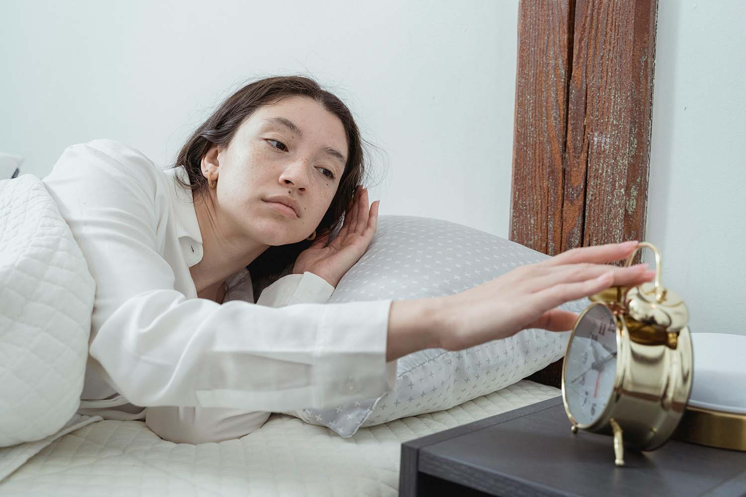 woman in bed, checking the time on her bedside clock