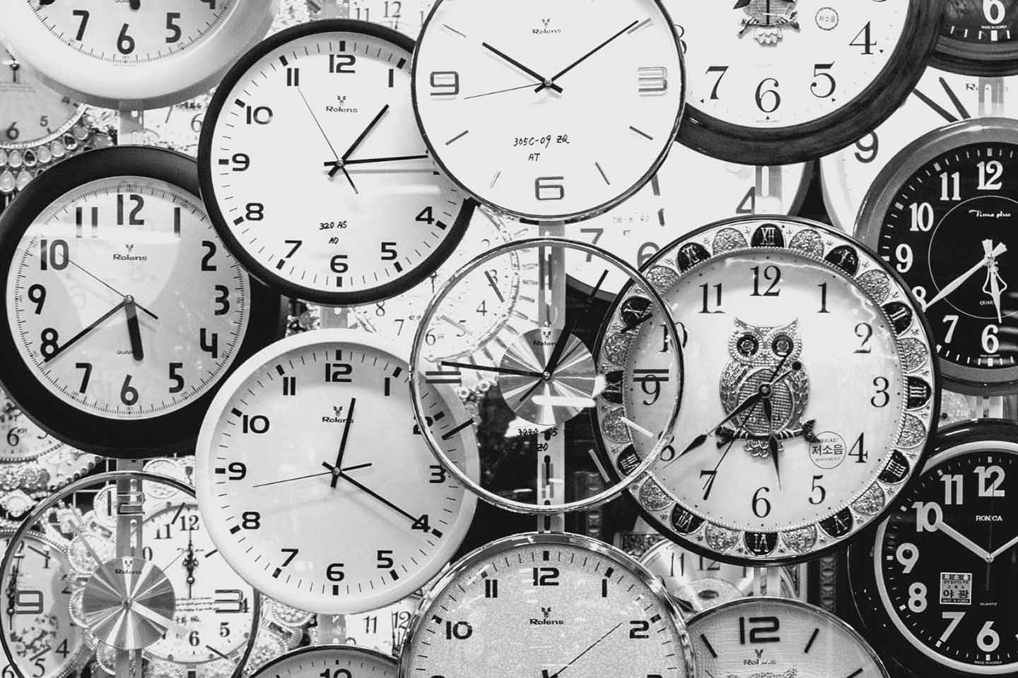 Several clocks overlapping on a wall in black and white shot.