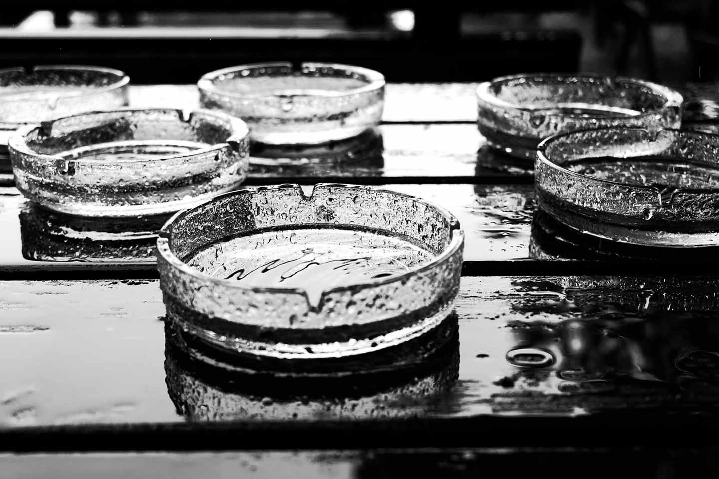 seven glass ashtrays on a wet table in the rain