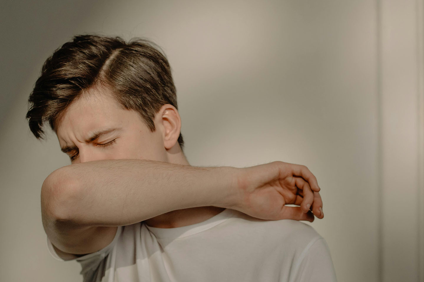 man in white tee shirt coughing into his elbow