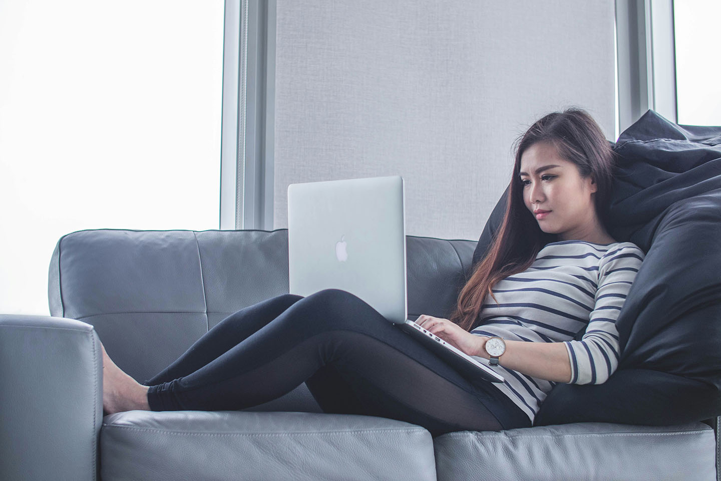 woman with long hair sitting on couch looking at MacBook laptop