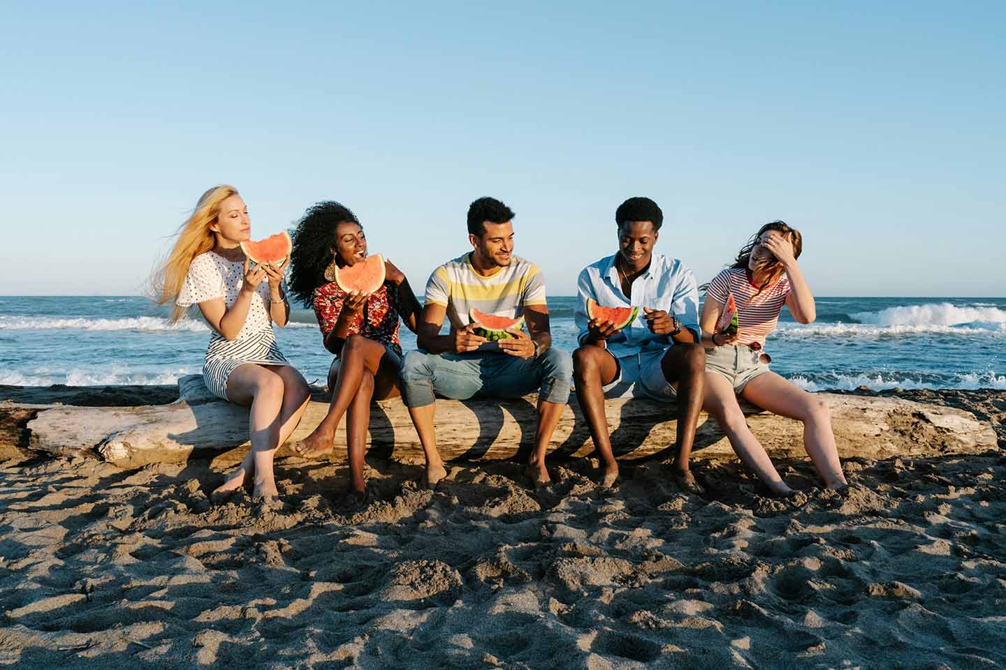 Group of friends eating watermelon on the beach