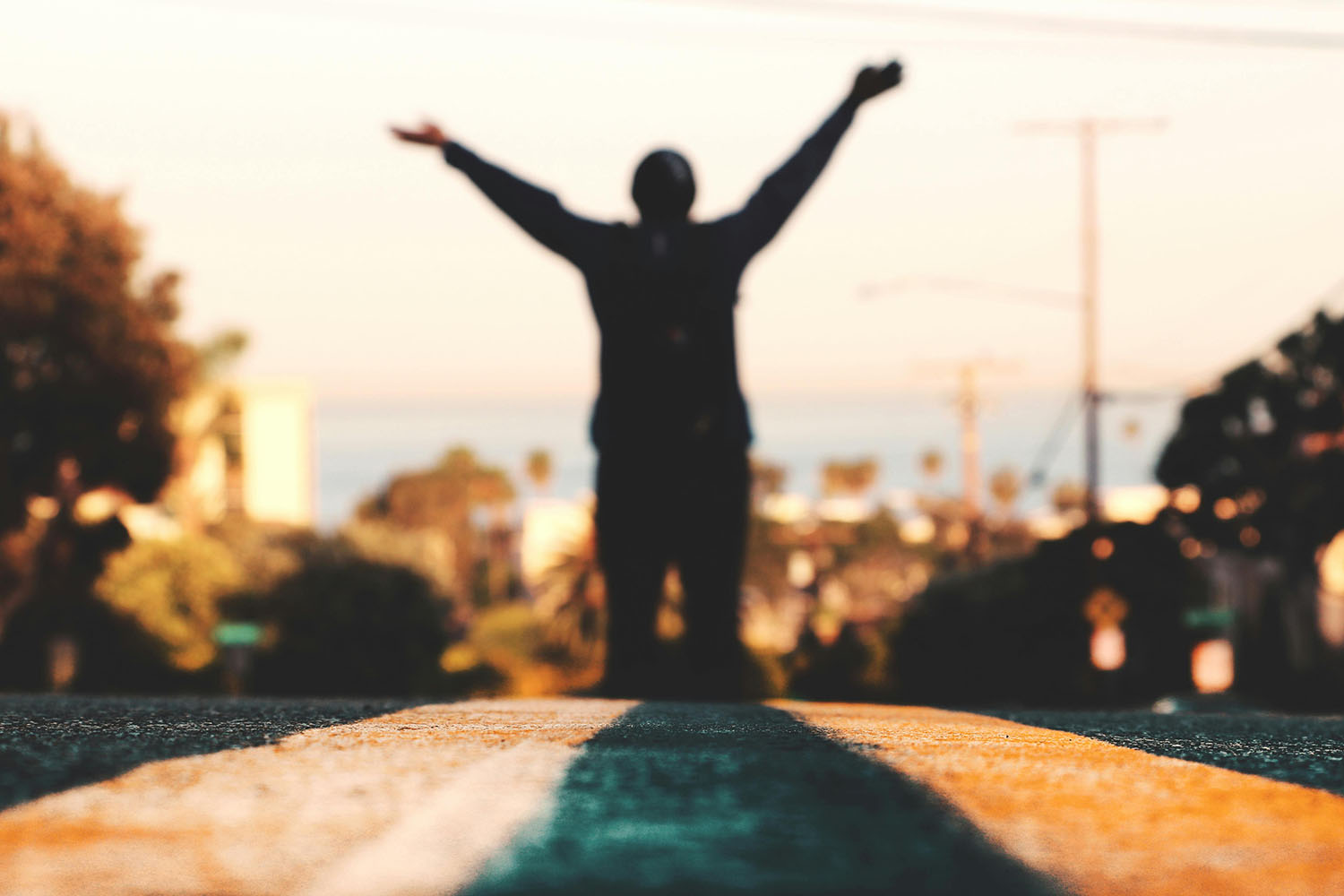 Silhouette of person raising their arms to the sky at sunset