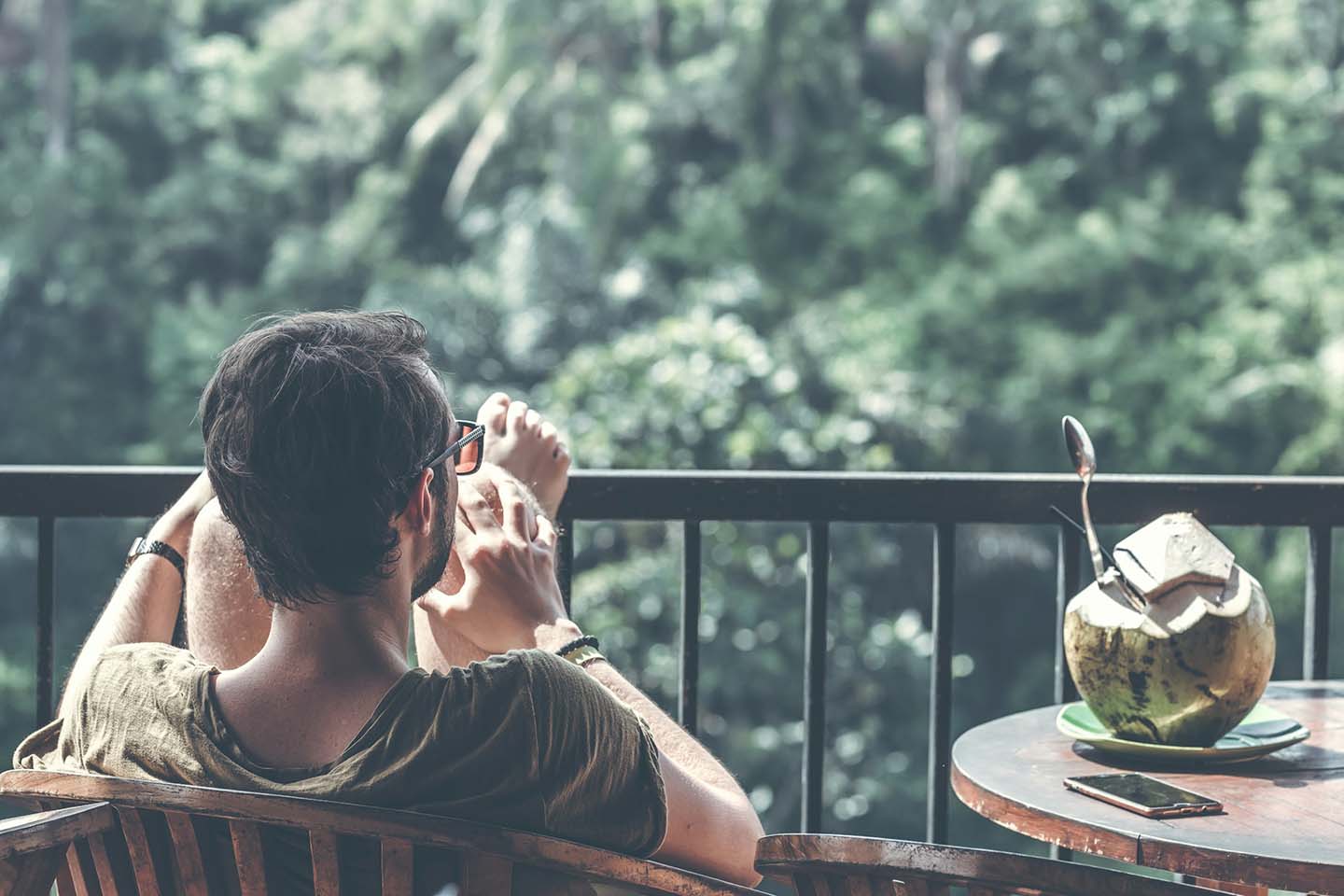 a man sitting on a chair near a table with open coconut while looking at trees