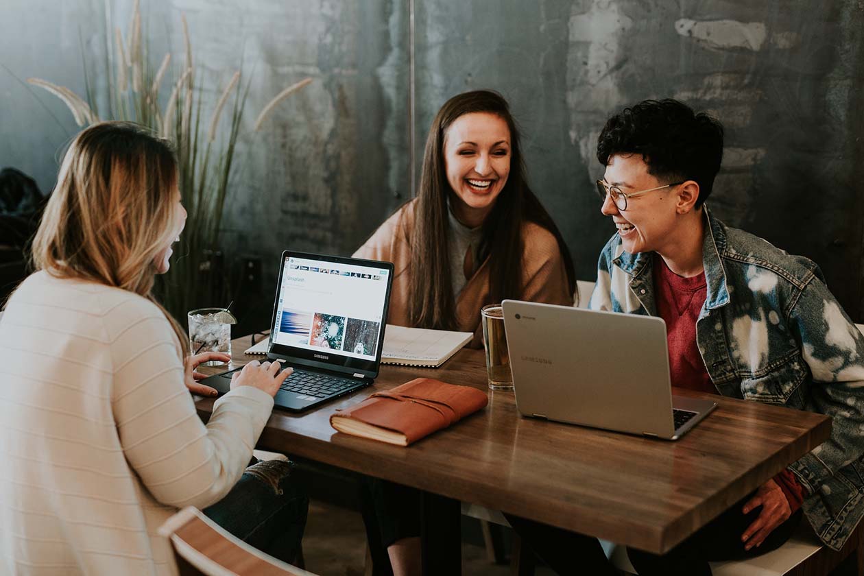 three people at a desk looking at their computers and laughing