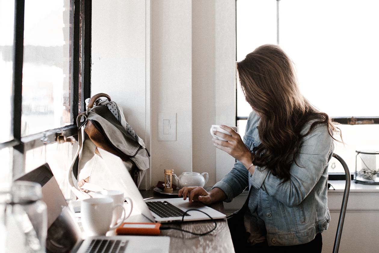 woman at a computer holding white ceramic teacup