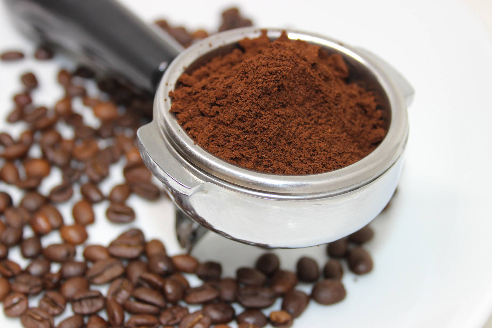 A pure coffee powder in a stainless steel detachable portafilter with coffee beans scattered in the background.
