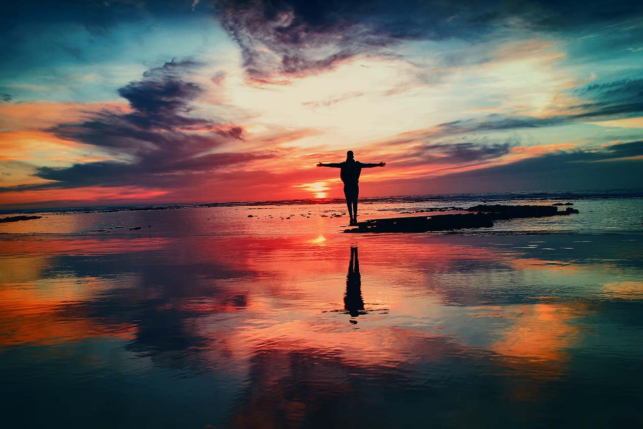 silhouette of a person with outstretched arms looking at a sunset