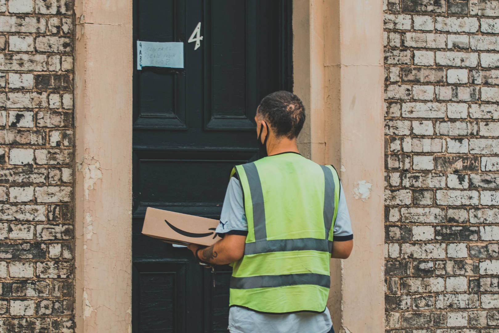 An Amazon delivery man holding a box waiting at the customer's door.