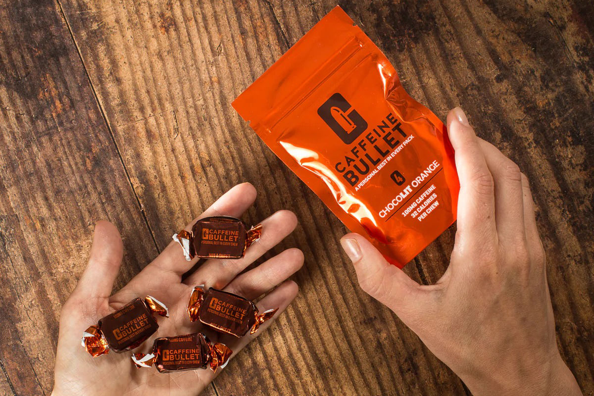 A person holding a resealable pack of Caffeine Bullet in Chocolit Orange flavor on right hand and holding four Caffeine Bullet candies on the left hand.