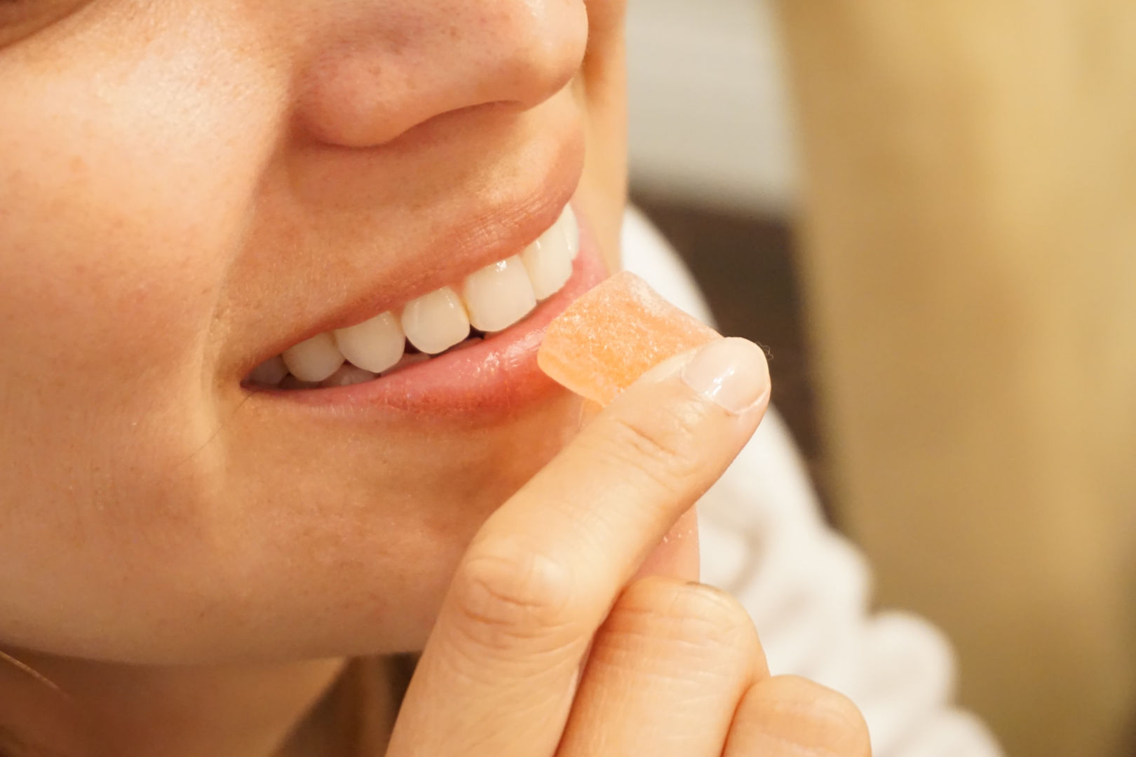 A smiling woman holding an orange candy to her mouth.