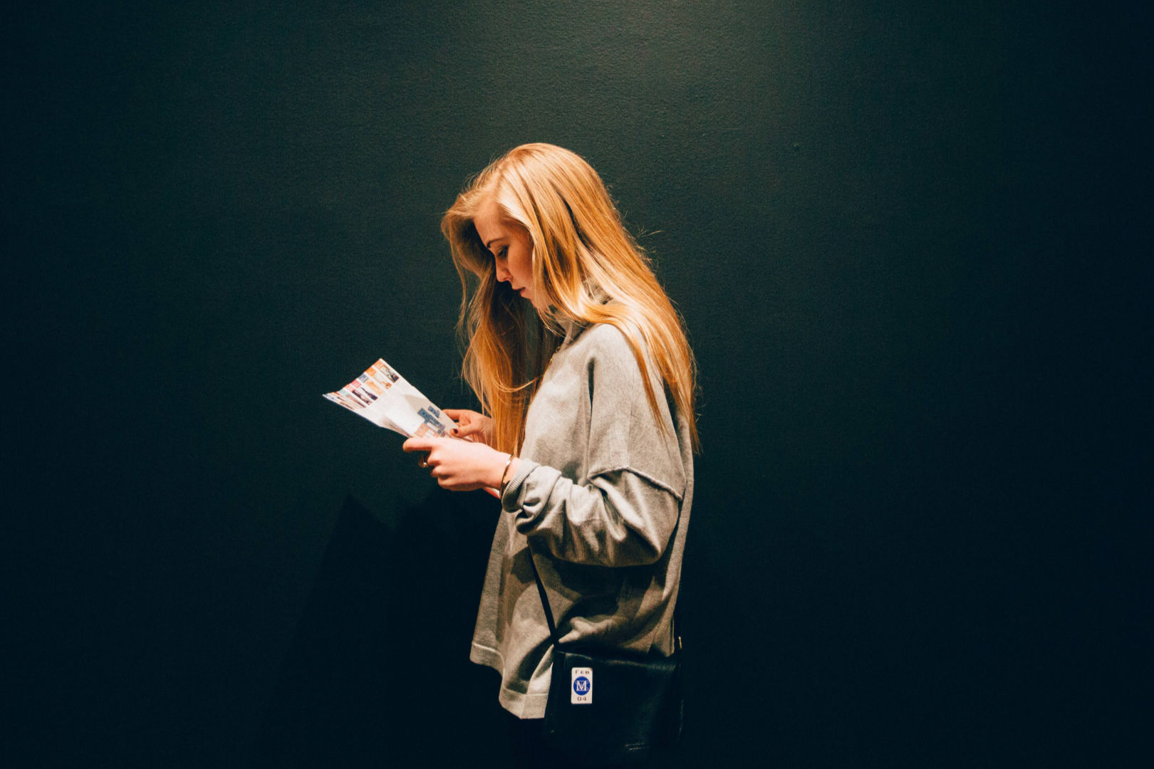 A woman reading a magazine under a bright light in front of a dark wall.