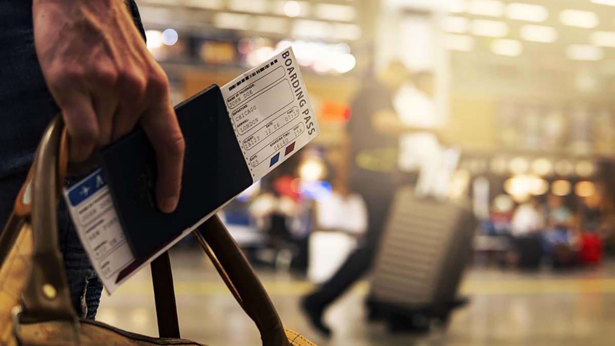 Traveler in an airport, holding a carry-on bag and a boarding pass.