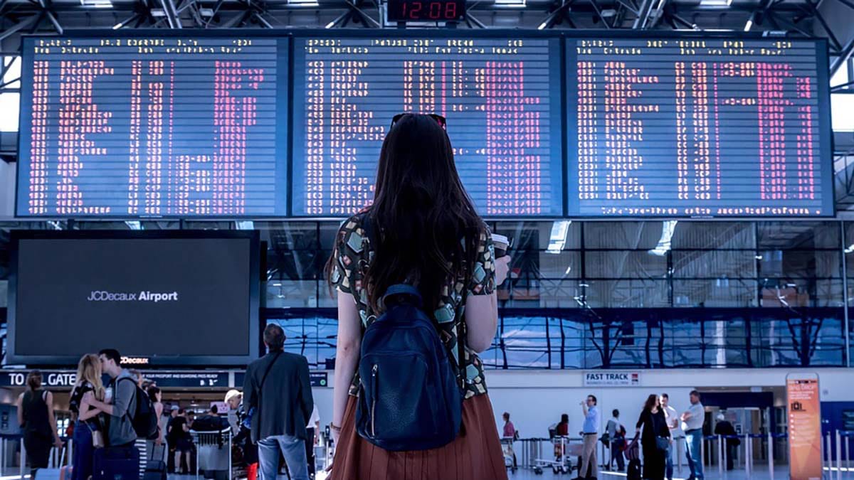 Woman standing in an airport terminal carrying a backpack.