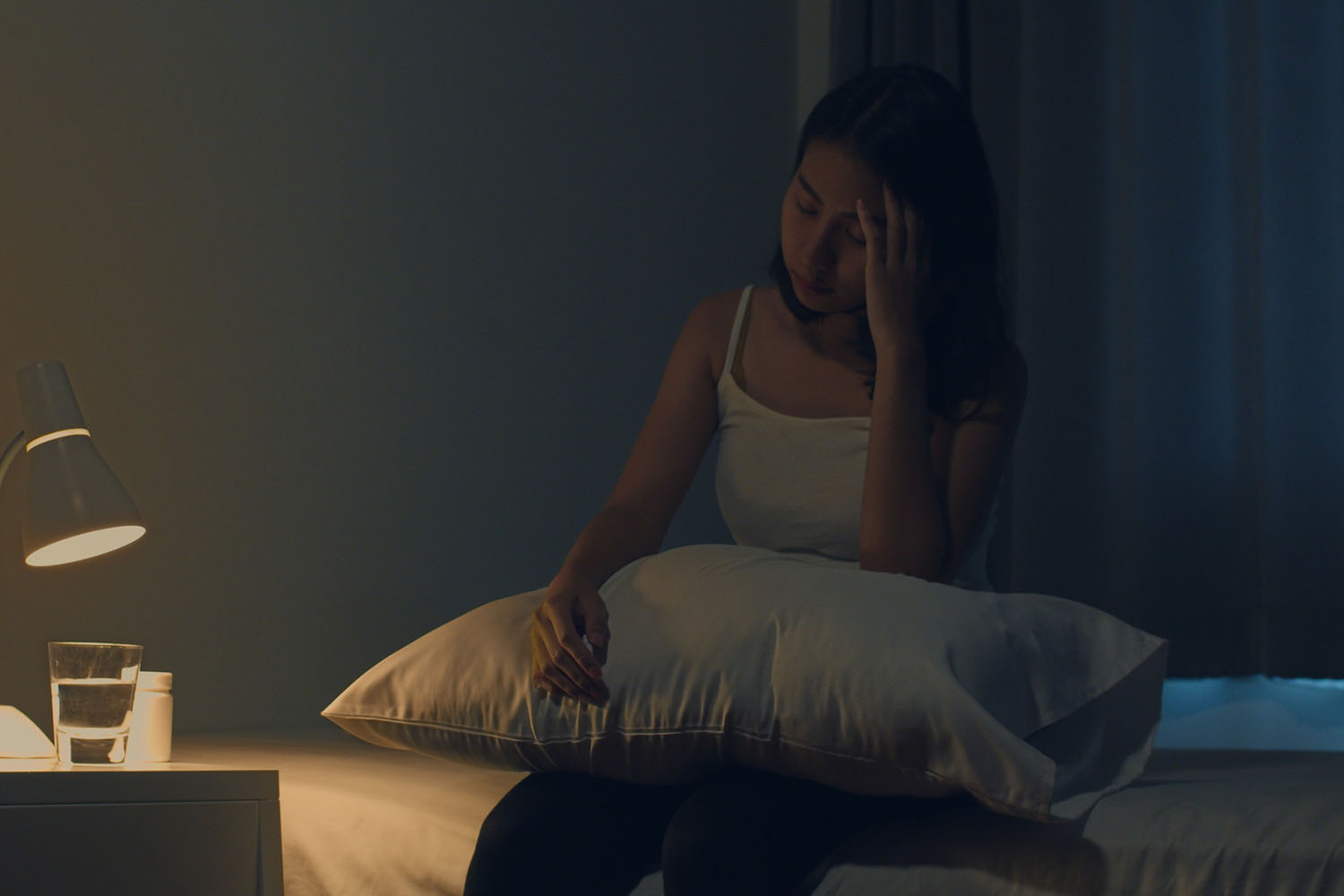Tired-looking woman sitting in a dark room, reaching for sleeping pills