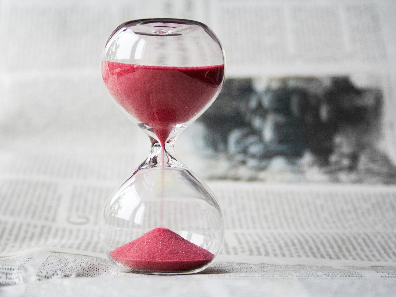 hourglass with pink sand placed on a newspaper print.