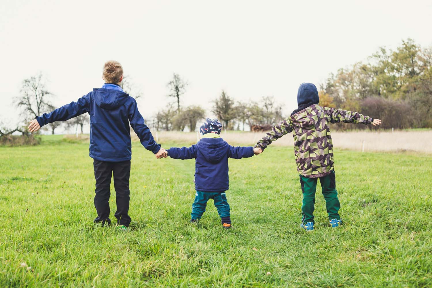 three children holding hands while standing on a lawn