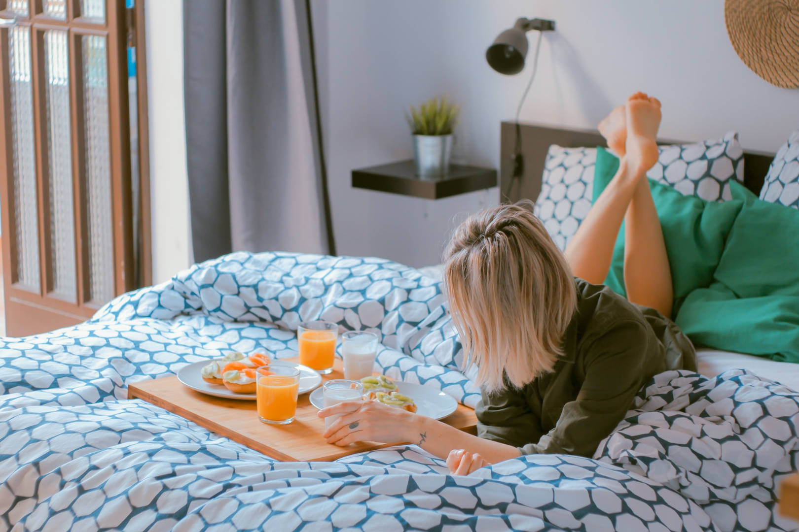 A woman lying on her stomach in bed with a breakfast tray of food.