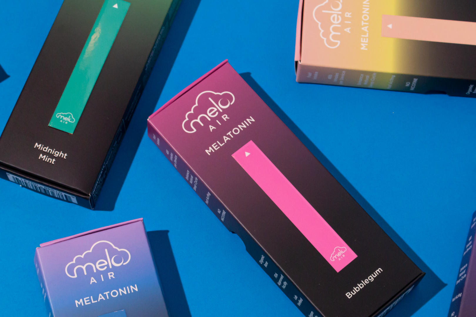 Boxes of MELO Air Melatonin Diffusers scattered on a blue surface.