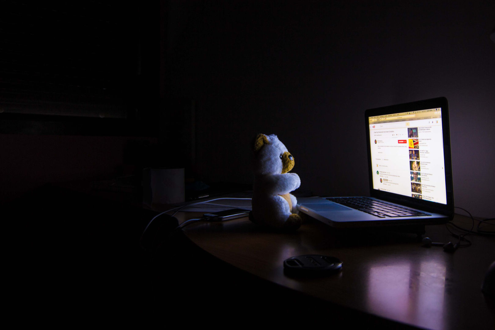 A laptop beside a small teddy bear late at night.