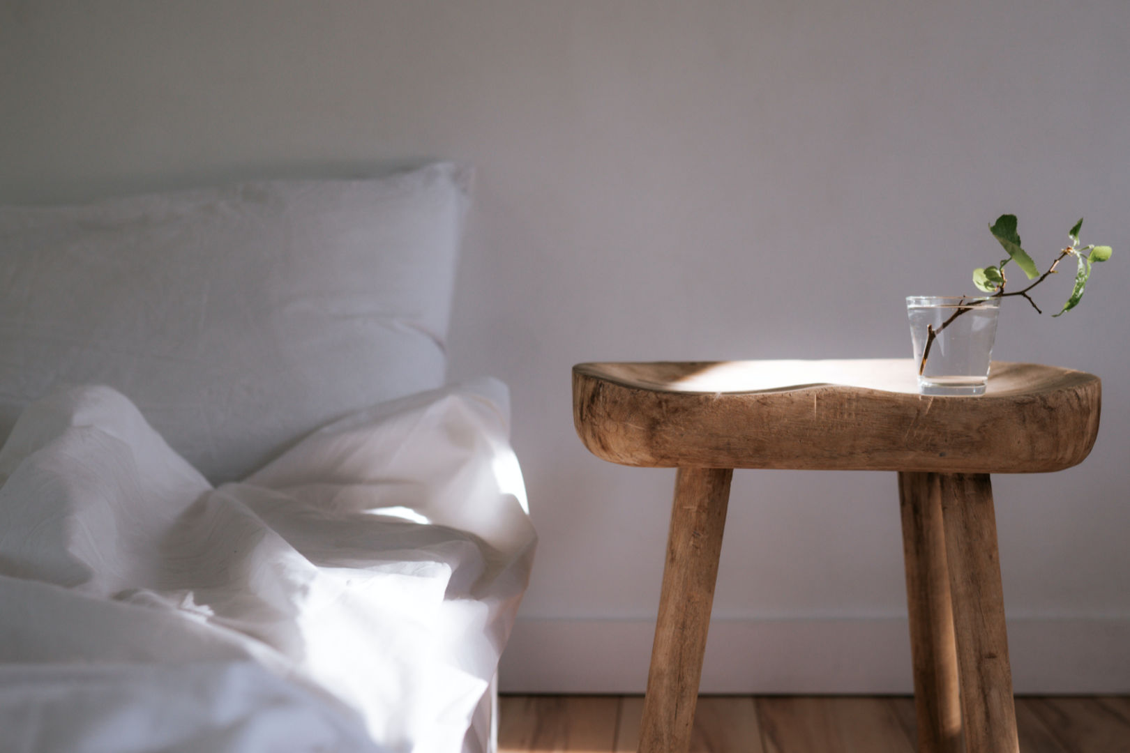 A white bed and a bedside table with a plant on top.