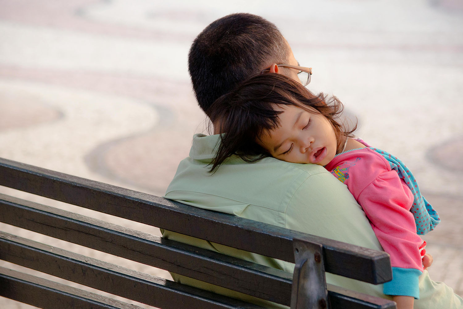 A man holding a sleeping child on a bench