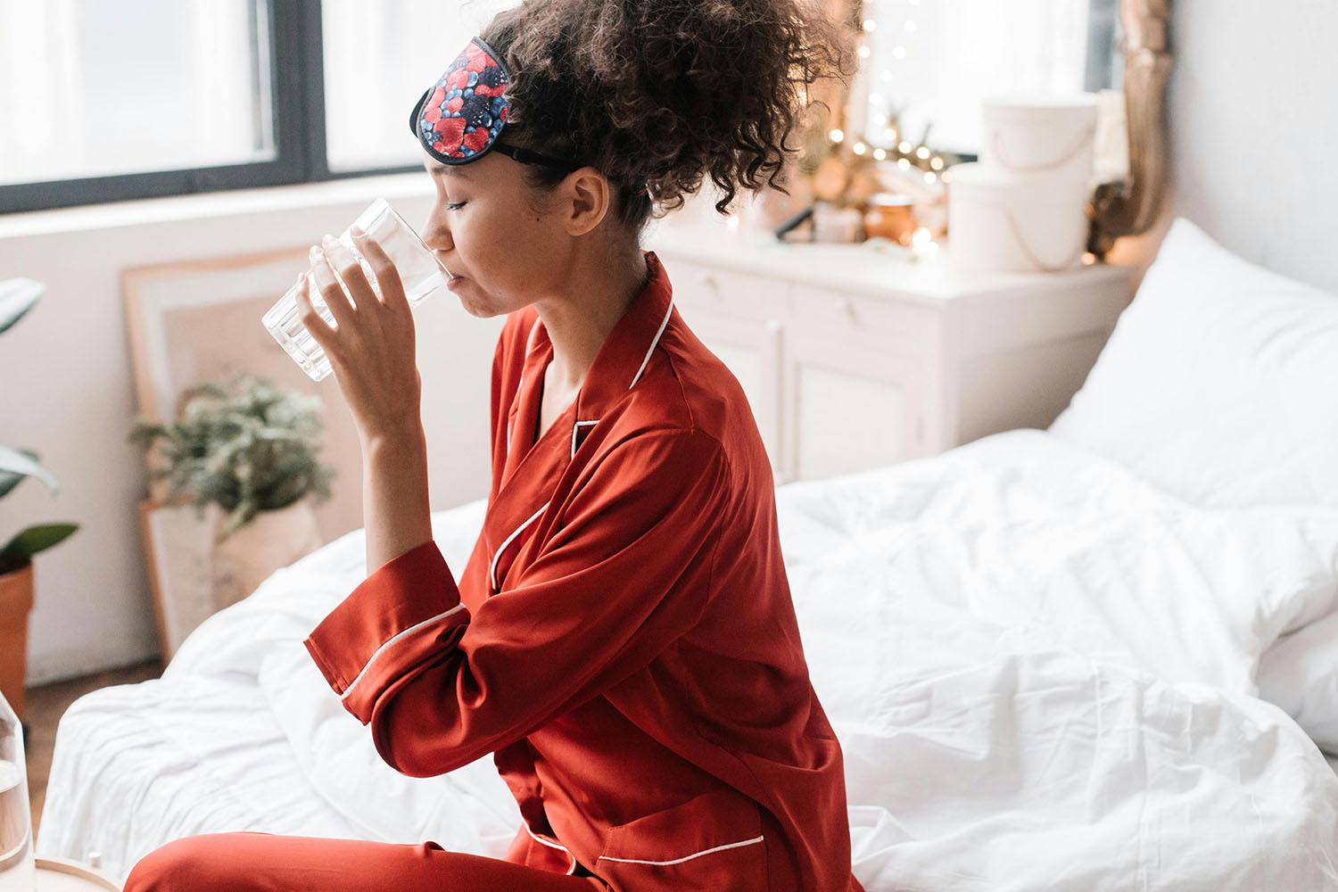 A woman sitting on a bed drinking a glass of water